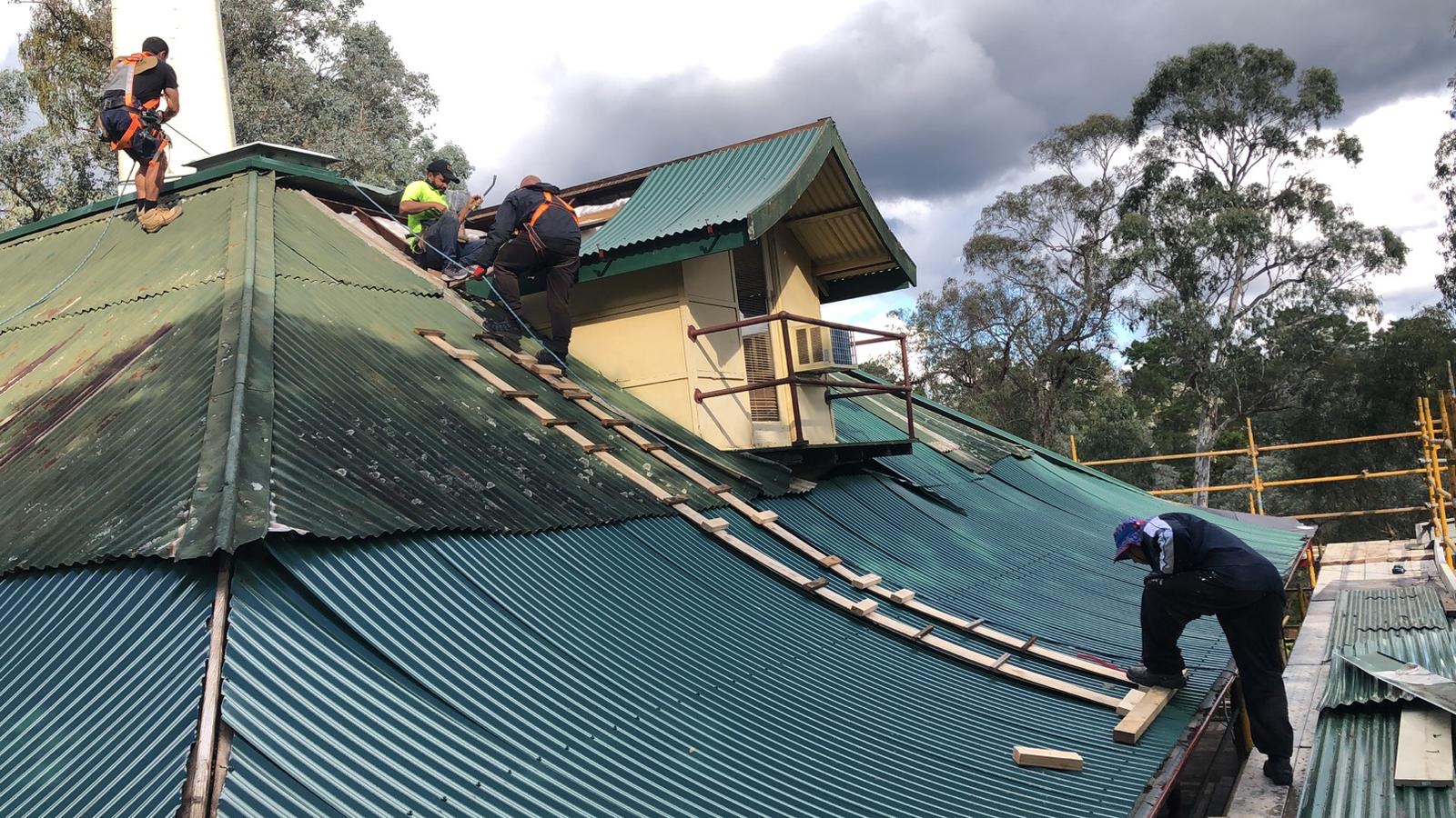 Green corrugated roof restoration with rope-access crew